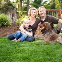 family of three and dog outside sitting on the grass