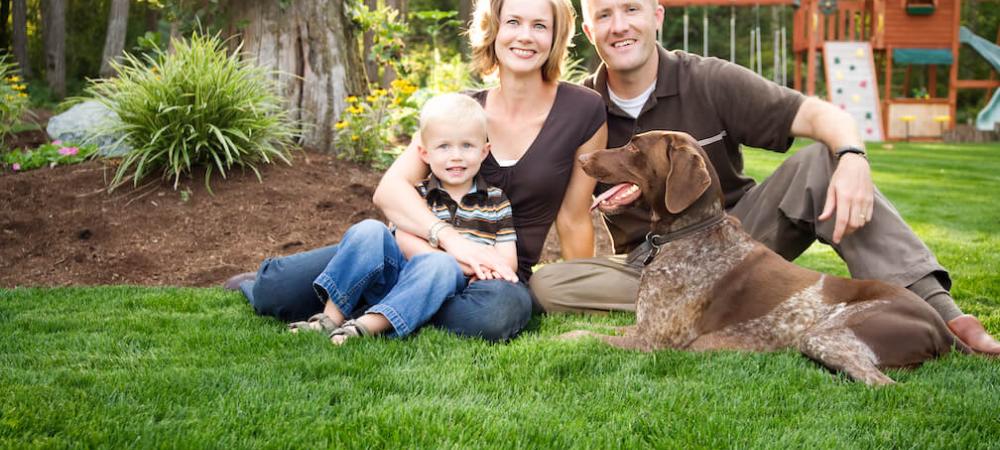 family of three and dog outside sitting on the grass